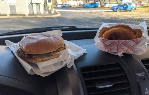 A cheeseburger and a container of onion rings placed on the dashboard of a car.