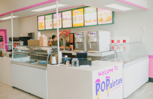 Bright ice cream shop interior with a counter, menu boards, and a staff member preparing orders.