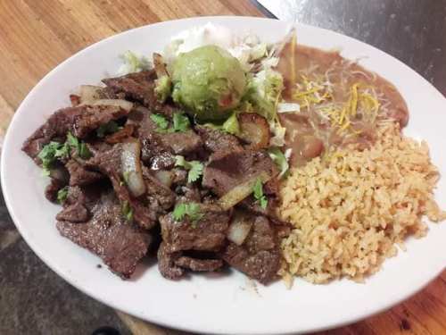 A plate of grilled beef with onions, guacamole, rice, refried beans, and shredded cheese, garnished with lettuce.