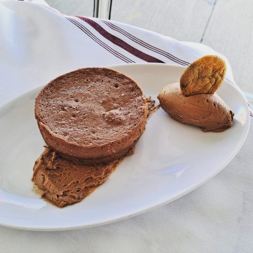 A plate featuring a round chocolate mousse cake, a scoop of chocolate mousse, and a cookie on the side.
