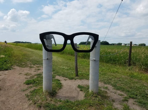 Oversized black glasses sculpture on two posts, set against a grassy field and blue sky.
