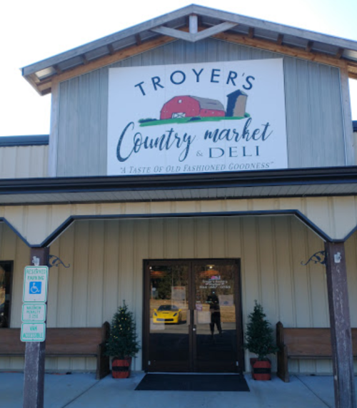 Front view of Troyer's Country Market & Deli, featuring a sign and decorative plants by the entrance.