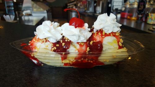 A delicious ice cream sundae with three scoops, topped with whipped cream, cherries, and nuts in a clear dish.