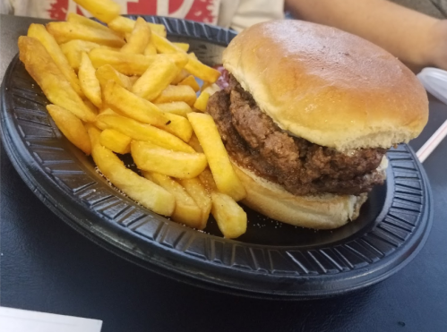 A plate with a hamburger and a side of golden French fries on a black tray.
