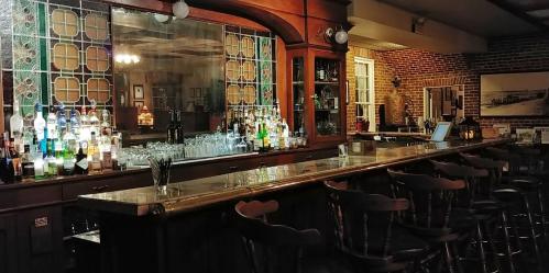 A dimly lit bar with a polished wooden counter, shelves of liquor, and vintage decor.