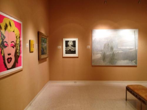 Art gallery interior featuring colorful and diverse artworks on the walls, including a portrait and landscape pieces.
