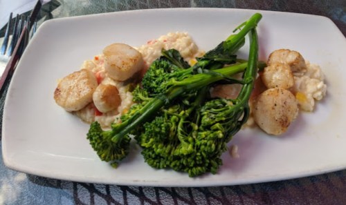 A plate featuring seared scallops, creamy risotto, and sautéed broccolini.