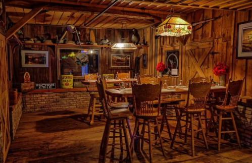 Cozy wooden dining room with a large table, chairs, and rustic decor, illuminated by warm lighting.