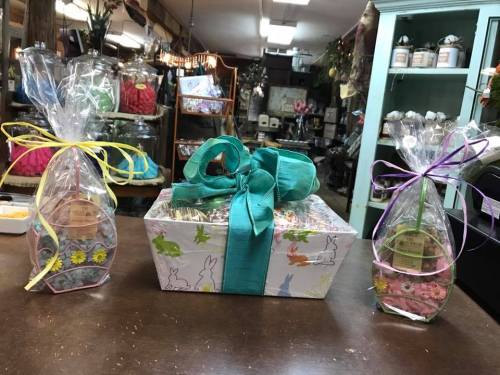 Three gift baskets wrapped in cellophane with colorful ribbons, displayed on a wooden table in a shop.