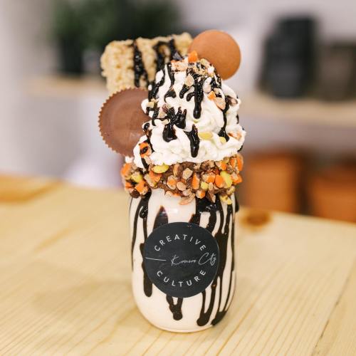 A decadent milkshake topped with whipped cream, chocolate drizzle, candy pieces, and cookies in a jar.