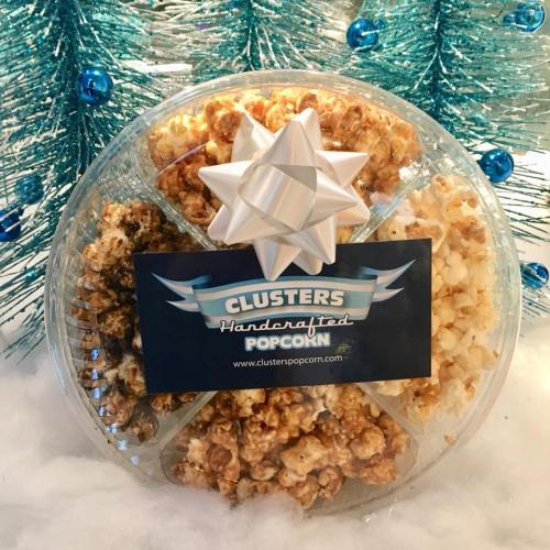 A round gift box of handcrafted popcorn with a bow, surrounded by blue tinsel and white fluffy decor.