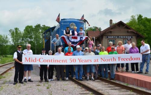 Group photo at North Freedom station celebrating 50 years of Mid-Continent Railway, with a train in the background.