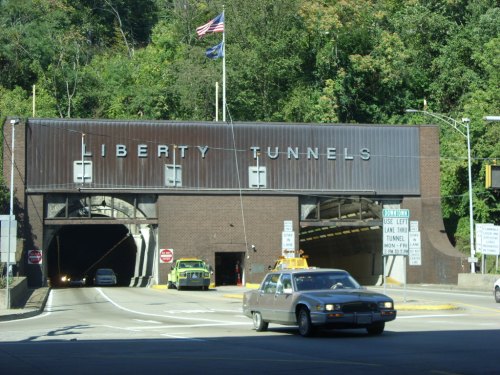 Entrance to the Liberty Tunnels, with vehicles approaching and greenery in the background. American flag visible.