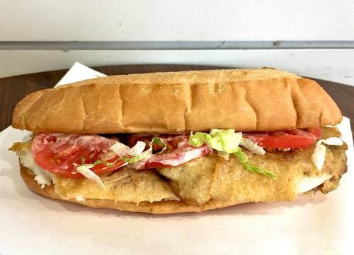 A sandwich with a crispy fish fillet, lettuce, and tomato slices on a toasted bun, served on a white napkin.