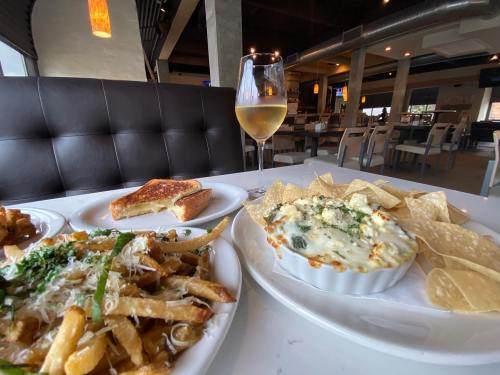 A table setting featuring a glass of white wine, a plate of cheesy dip with chips, fries, and a grilled cheese sandwich.