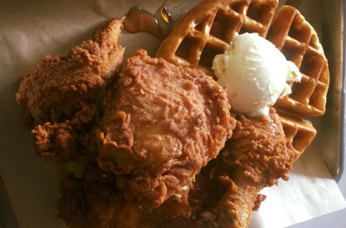 A plate of crispy fried chicken served with a waffle and a scoop of ice cream, drizzled with syrup.