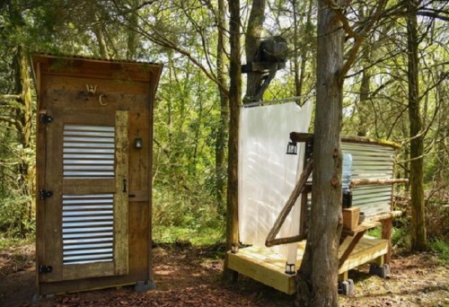 Outdoor bathroom setup featuring a wooden toilet and a shower area surrounded by trees.