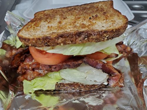 A hearty sandwich with toasted bread, bacon, lettuce, and tomato, served in foil.