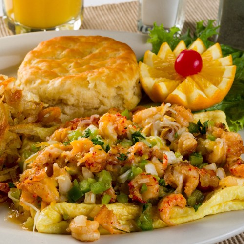 A plate of shrimp omelette with vegetables, a biscuit, hash browns, and orange slices garnished with a cherry.