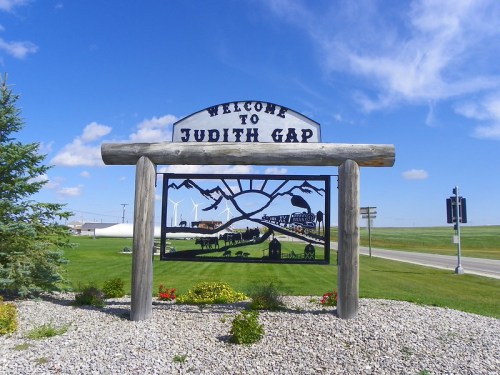 Welcome sign for Judith Gap, featuring a metal cutout of mountains and local scenery against a blue sky.