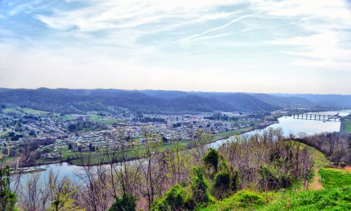 A scenic view of a river winding through a valley, with a small town and hills in the background under a clear sky.