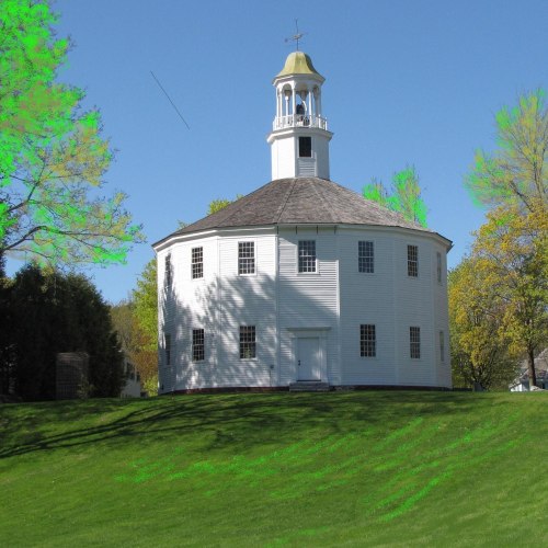 A round white building with a cupola, surrounded by green grass and trees under a clear blue sky.