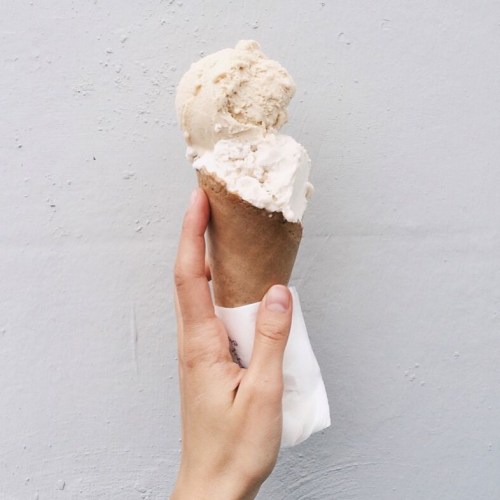 A hand holding a cone with two scoops of ice cream against a light gray background.