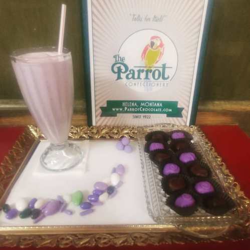 A milkshake and a tray of assorted chocolates on a decorative platter, with a sign for The Parrot Confectionery.