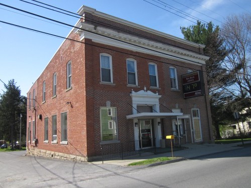 A brick building with a white entrance, featuring a sign displaying the time and an ATM, surrounded by trees.