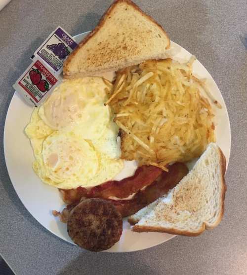 A plate of breakfast featuring eggs, hash browns, bacon, sausage, and toast with jelly packets on the side.