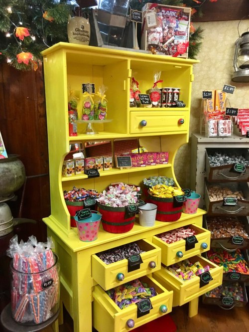 A bright yellow display cabinet filled with colorful candies and treats in baskets and jars.