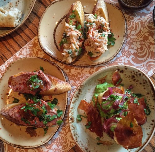 Three plates of gourmet appetizers featuring toasted bread topped with various spreads, meats, and garnishes.