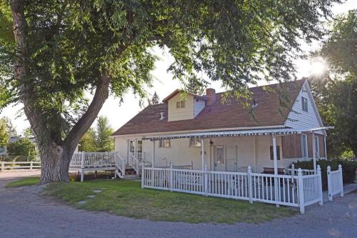 A charming white house with a brown roof, surrounded by greenery and a white picket fence, under a sunny sky.