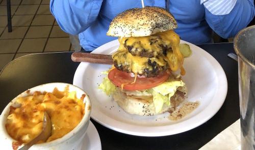 A towering cheeseburger with two patties, lettuce, tomato, and a side of cheesy macaroni on a plate.