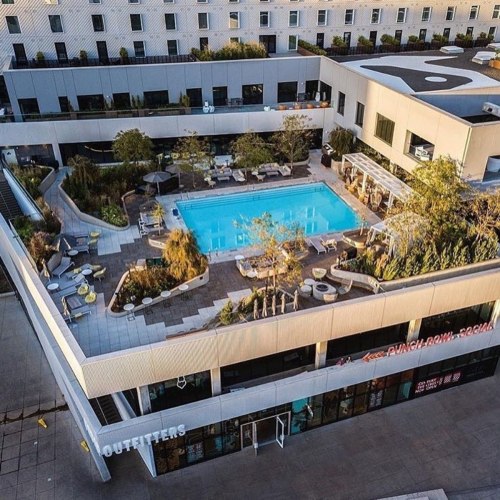 Aerial view of a modern hotel with a pool, lounge chairs, and outdoor seating areas surrounded by greenery.