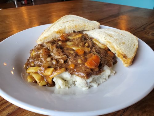 A plate of mashed potatoes topped with savory beef stew and served with two slices of toasted bread.