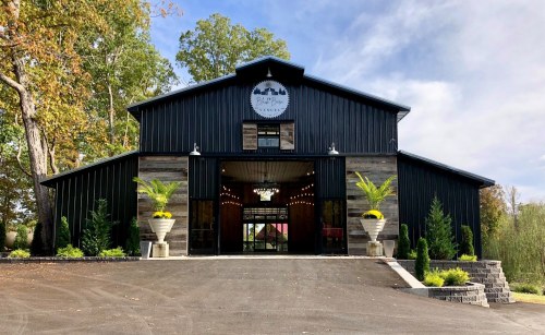A modern barn-style building with a black exterior, large entrance, and decorative plants on either side.