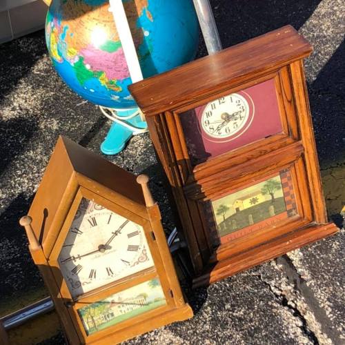 Two vintage clocks with different designs, alongside a colorful globe, on a sunny outdoor surface.