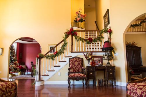 A festive living room with a staircase, decorated with garlands and a Christmas tree in the background.