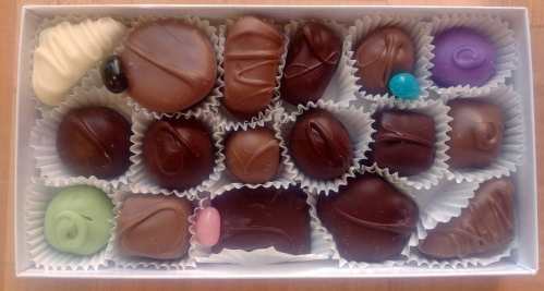 A box of assorted chocolates in various shapes and colors, arranged neatly in paper liners.