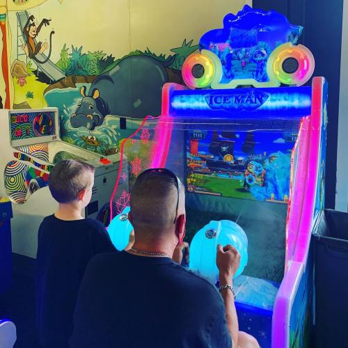 A child and an adult play an arcade game called "Iceman," with colorful lights and a vibrant background.