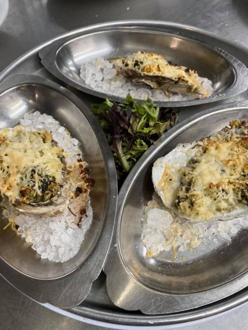 Three baked oysters on a metal platter, garnished with greens and served on a bed of ice.