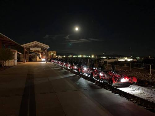 A row of illuminated go-karts on a track at night, with a full moon and distant lights in the background.