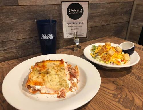 A plate of lasagna with a side salad and a drink on a table at a family restaurant.