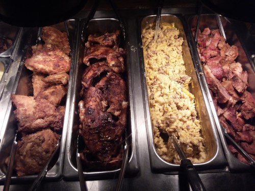 A buffet display featuring various meats and a side of macaroni and cheese in metal trays.