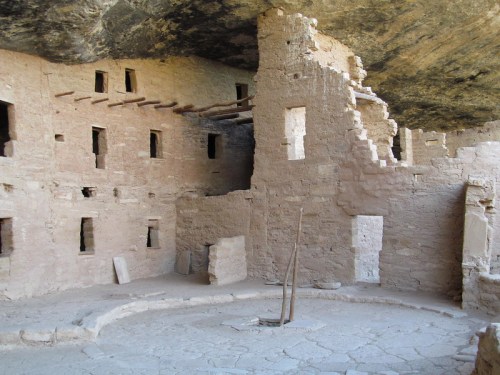 Ancient cliff dwelling with stone walls and wooden beams, set in a rocky cave.