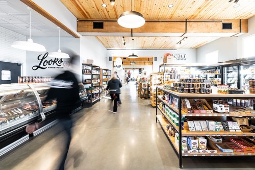A bright marketplace interior with wooden beams, shelves of products, and shoppers moving through the aisles.