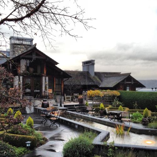 A rustic building with a stone facade, surrounded by greenery and outdoor seating, under a cloudy sky.