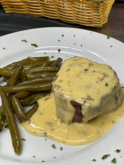 A plate featuring a meat dish topped with creamy sauce, accompanied by green beans and garnished with herbs.