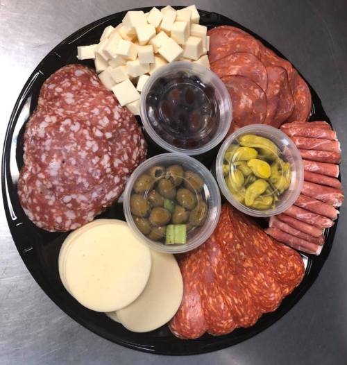 A platter featuring assorted meats, cheeses, olives, and pickles arranged in circular sections.